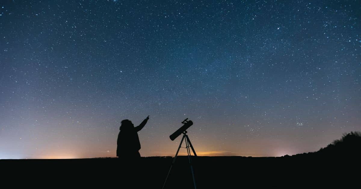 Pessoa montando um telescópio em um campo à noite.